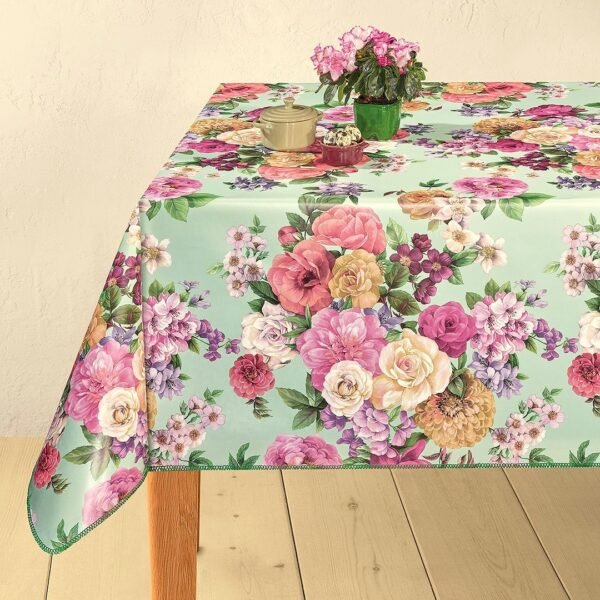 A wipe-clean tablecloth featuring a vibrant floral pattern with pink, yellow, and white flowers on a light green background, displayed on a wooden table with decorative items on top